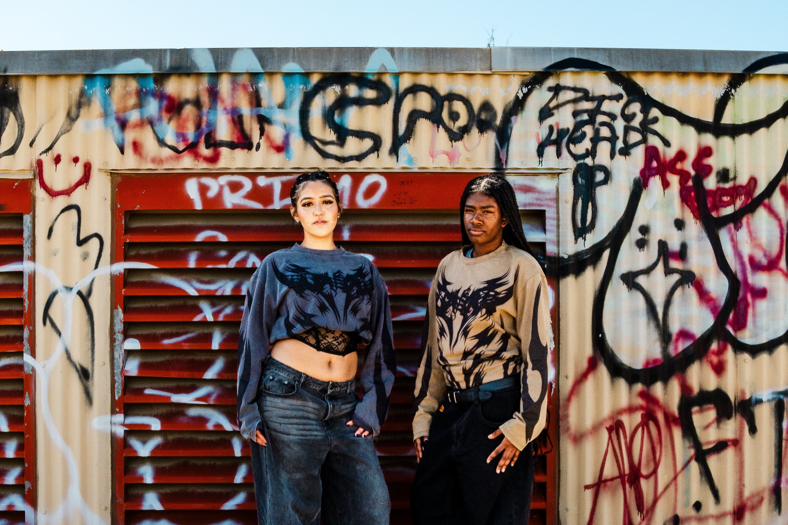 Two people standing in front of a graffiti-covered wall.